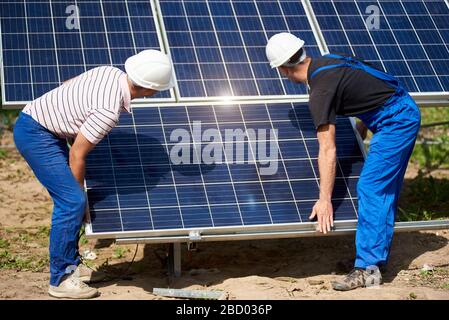 Zwei Techniker, die am sonnigen Sommertag in der ländlichen Umgebung ein voltaisches, eigenständiges Solarpanel-System installieren. Regenerative ökologische billige umweltfreundliche Energieerzeugung Konzept. Stockfoto