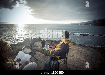 Digitale Nomade und Freiheit vom Lebensstil der Büroarbeit - ein Paar Reisende genießen die Arbeit im Freien auf der Klippe mit Blick auf den Ozean und Stockfoto