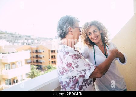 Zwei verschiedene Altersfrauen berühren zuhause auf der Terrasse mit Blick auf die Stadt die Stanze - Konzept von Team und Freundschaft oder Mutter und Tochter adu Stockfoto
