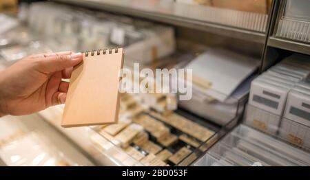 Leeres braunes Papierblatt mit Notizbuchpapier ohne Zeile zum Schreiben von Textnotizen. Die Hand eines Weibchens hielt ein Buch mit leerem Papier auf einem braunen Korkbezug Stockfoto