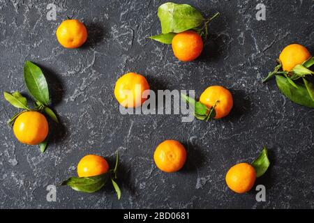 Frische organische Tangerinen mit Blättern auf schwarzem Stein- oder Betongrund. Draufsicht Stockfoto