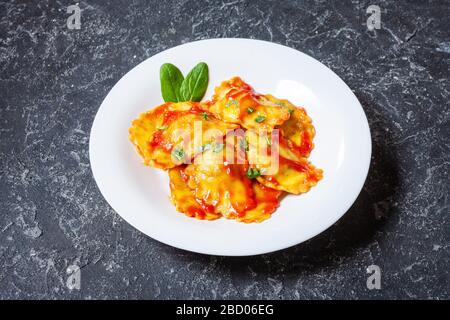 Ravioli mit Tomatensauce und Basilikum auf dunklem Steingrund. Köstliche Pasta Stockfoto