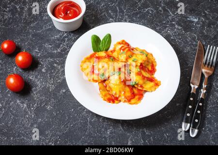 Ravioli mit Tomatensauce und Basilikum auf dunklem Steingrund. Köstliche Pasta Stockfoto