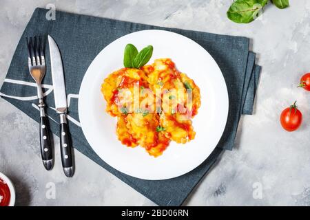 Ravioli mit Tomatensoße und Basilikum auf Betongrund. Köstliche Pasta. Draufsicht Stockfoto
