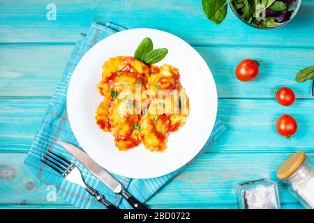 Ravioli mit Tomatensauce und Basilikum auf blauem Holzhintergrund. Köstliche Pasta. Draufsicht Stockfoto