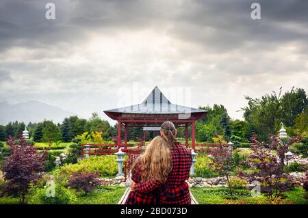 Junges Paar in rot Karo-hemden umarmen und mit Blick auf die japanische Pagode Garten bei bedecktem Himmel Stockfoto