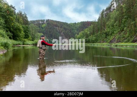 Kaukasischer älterer Fischer mit Angelrute im Flusswasser. Jagd und Hobbysport. Stockfoto