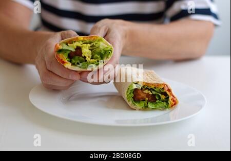 Mittelteil der Frau, die Tortilla mit gebratenem Hühnerfleisch und Gemüse hält Stockfoto