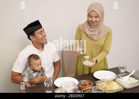 Schöne Hijab-Frau, die ihrem Mann etwas Essen serviert, während sie abends das Fasten brach Stockfoto