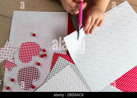 Die Hand des Kindes macht Grußkarte mit Herz. Dekoration auf dem Hintergrund. Hobbykonzept. Handgefertigt. Heimwerkerkonzept für Kinder. Stockfoto