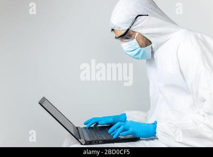 Forscher, der mit seinem Laptop in Covid-19 Coronavirus Schutzkleidung arbeitet Stockfoto