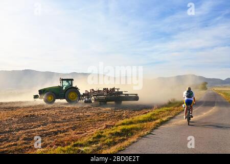 Traktor arbeitet auf dem landwirtschaftlichen Feld in Staub während des ruhigen Herbstabends und mit dem Fahrrad Stockfoto