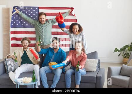 Multiethnische Gruppe von Freunden, die Sportmatches beobachten und emotional jubeln, während sie die amerikanische Flagge halten, kopieren Raum Stockfoto