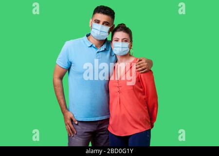 Porträt eines jungen, attraktiven Familienpaares mit chirurgischer medizinischer Maske, die zusammen steht, Kamera mit Lächeln umarmte und ansah, starke Beziehungen. Stockfoto