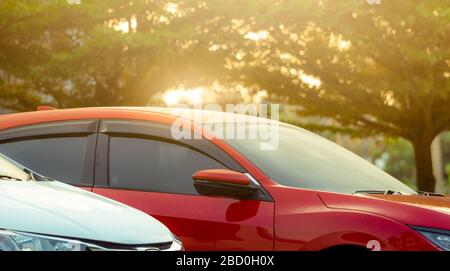 In der Nähe geparktes rotes SUV-Auto auf dem Parkplatz des Einkaufszentrums oder Büros im Freien. Luxusauto parkt in der Nähe des grünen Baums auf dem Parkplatz mit dem Morgen Stockfoto