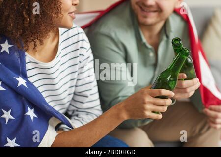Nahaufnahme von gemischten jungen Paaren, die Bierflaschen klinken, während sie amerikanische Flagge tragen, Kopierraum Stockfoto