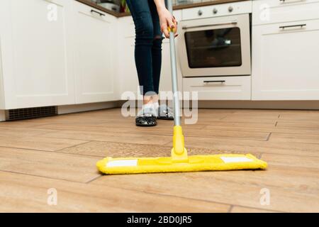 Das Zimmer war eine Hausfrau, die zu Hause den Boden putzte. Schöne Frau wäscht Holzböden aus einem Laminat in einer hellen Küche. Stockfoto