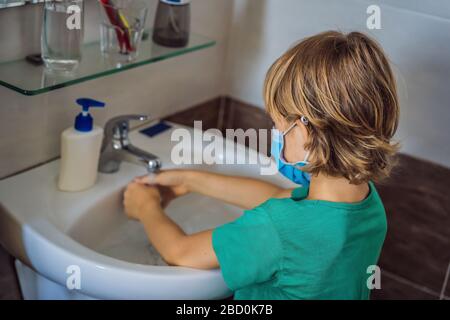 Der Junge wäscht seine Hände mit Seife. Junge in einer medizinischen Maske wegen Coronavirus. Pandemie. Bleiben Sie zu Hause. Waschen Sie Ihre Hände Stockfoto