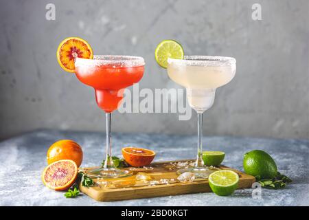 Gefrorene Limette margarita und blutrange margarita Cocktailmischung in salzriemenden Brillen, die mit Limetten und Orange garniert werden. Konzentrieren Sie sich auf das Zitrus-sli Stockfoto