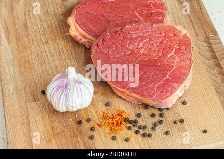 Rohes Rindfleisch steaks auf einem Holzbrett mit Knoblauch, schwarzem Pfeffer und Safran. Köstliches Mittagskonzept Stockfoto