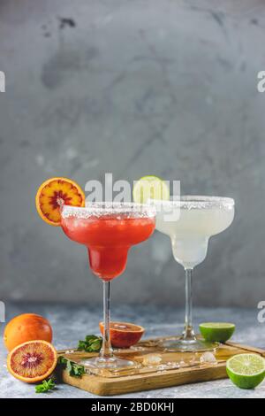 Gefrorene Limette margarita und blutrange margarita Cocktailmischung in salzriemenden Brillen, die mit Limetten und Orange garniert werden. Konzentrieren Sie sich auf das Zitrus-sli Stockfoto