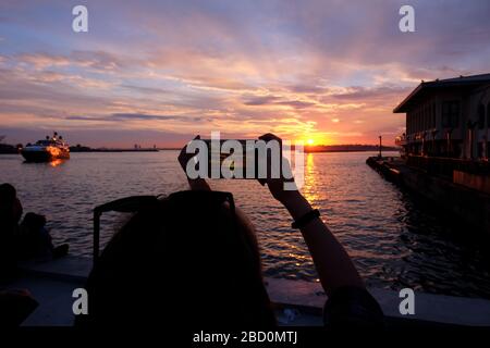 Junge Frau fotografiert mit einem Smartphone an der Küste von Istanbul, Kadikoy bei Sonnenuntergang. Stockfoto