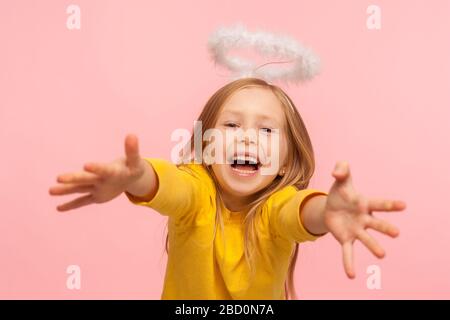 Freute glückliches kleines Mädchen mit Engelhalos, das mit Glück schreit und in die Kamera greift, um eng zu umarmen, sehr froh, Sie zu sehen. Tochter Mi Stockfoto