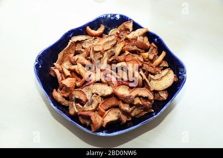 Dehydrierte Äpfel Späne auf Platte, Draufsicht. Getrocknete Apfelspäne in einer quadratischen Glasplatte . Getrocknete apfelscheiben in der blauen Platte des Woodenls isoliert auf weiß . Stockfoto