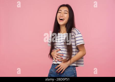 Witziger Witz! Porträt eines fröhlichen optimistischen Mädchens mit langen Haaren im gestreiften T-Shirt, das Bauch hält und laut lacht, amüsiert von albern lustigen Anecdot Stockfoto