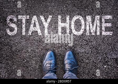 Nachricht bleib zu Hause geschrieben auf Asphalt Straße mit Beinen und Schuhen Stockfoto
