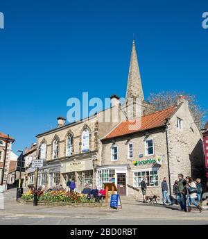 Käufer und Besucher entspannen sich bei Sonnenschein in Birdgate, dem obersten Ende des Marktplatzes in Pickering, North Yorkshire Stockfoto