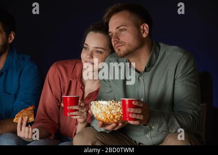 Porträt eines erwachsenen Ehepaares, das zu Hause Filme beim Essen von Snacks und Popcorn auf dem Sofa im dunklen Zimmer sieht Stockfoto