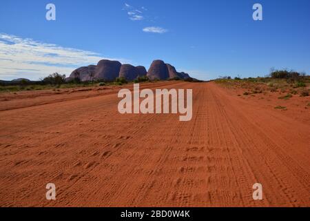 Northern Territory, Australien: Tief verwinkelte Weitwinkelansicht der roten Staubstraße im Outback mit der Felsformation von Kata Tjuta oder Olgas im Bac Stockfoto