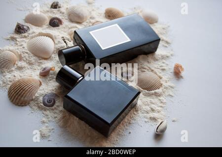 Zwei Parfümflaschen aus dunklem Glas auf Sand mit Seashells Stockfoto