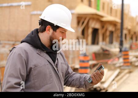 Kaukasischer Architekt beim Surfen mit dem Smartphone auf der Baustelle. Stockfoto