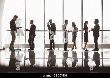 Silhouetten von Menschen gegen das Fenster. Ein Team junger Geschäftsleute, die in einem Büro zusammenarbeiten und miteinander kommunizieren. Unternehmens-Business und Stockfoto