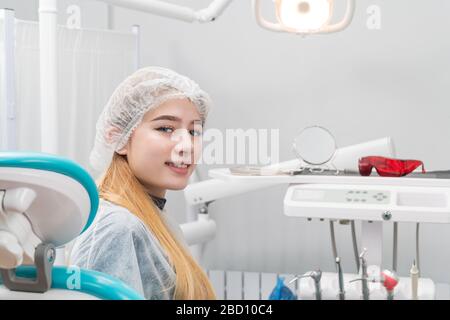 Patient - ein schönes Mädchen sitzt in einem Stuhl in der Zahnarztpraxis und dreht sich zurück Stockfoto
