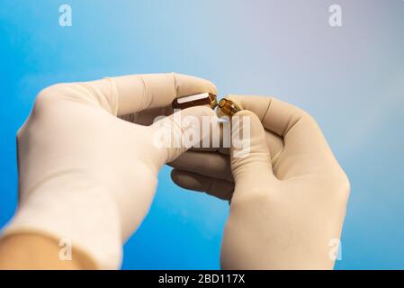 Nahaufnahme der Hände in Gummihandschuhen, die eine offene Ampulle mit einem Impfstoff halten Stockfoto