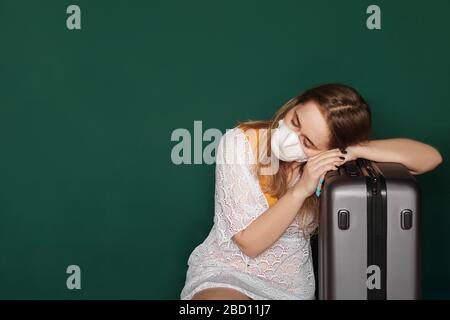 Müde Mädchen Reisende mit einer medizinischen Maske auf ihrem Gesicht warten auf verpasste, verspätete oder stornierte Flüge aufgrund eines Coronavirus. Covid-19 grüner Hintergrund Stockfoto