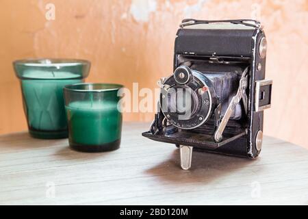 Alte Vintage-Kamera mit zwei schönen grünen Kerzen. Alte Vintage ruinierte Wand im Boden. Holzboden. Stockfoto