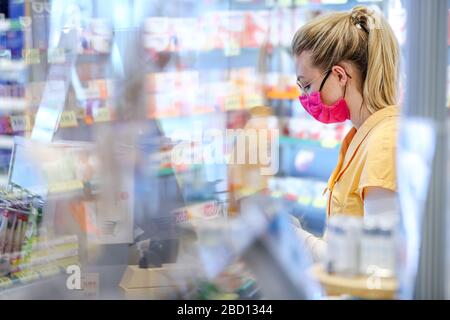 Leipzig, Deutschland. März 2020. Der Mitarbeiter einer Apotheke arbeitet mit einem selbst genähten Mundschutz. Um das 30-köpfige Team der Apotheke vor einer Infektion mit dem Corona-Virus zu schützen, reagierte der Chef frühzeitig. PLEXIGLAS wurde an die Kassen angehängt, und alle Mitarbeiter tragen auch eine Brille, die ebenfalls Schutz bieten soll. Zwei Mitarbeiter haben 90 Gesichtsmasken aus bunten Stoffen für ihre Kollegen genäht. Die Wäsche wird täglich in der Apotheke gewaschen. Kredit: Jan Woitas / dpa-Zentralbild / dpa / Alamy Live News Stockfoto