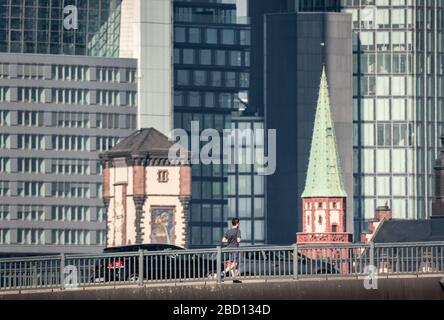 06. April 2020, Hessen, Frankfurt am Main: Ein Jogger (unten) überquert am Morgen vor der Kulisse der Stadt die Floßbrücke. Foto: Frank Rumpenhorst / dpa Stockfoto