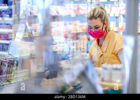 Leipzig, Deutschland. März 2020. Der Mitarbeiter einer Apotheke arbeitet mit einem selbst genähten Mundschutz. Um das 30-köpfige Team der Apotheke vor einer Infektion mit dem Corona-Virus zu schützen, reagierte der Chef frühzeitig. PLEXIGLAS wurde an die Kassen angehängt, und alle Mitarbeiter tragen auch eine Brille, die ebenfalls Schutz bieten soll. Zwei Mitarbeiter haben 90 Gesichtsmasken aus bunten Stoffen für ihre Kollegen genäht. Die Wäsche wird täglich in der Apotheke gewaschen. Kredit: Jan Woitas / dpa-Zentralbild / dpa / Alamy Live News Stockfoto