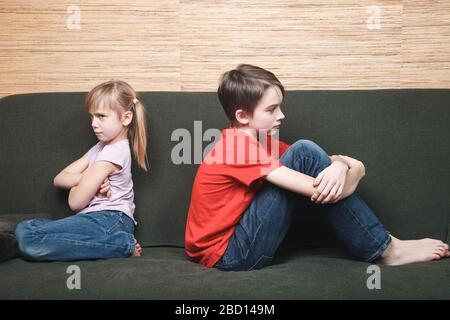 Frustrierte Geschwister sitzen auf einem Sofa, das zu Hause in Selbstisolation stecken blieb. Quarantäne und Sperrung von Schutzmaßnahmen gegen die Ausbreitung von Coronavirus Stockfoto