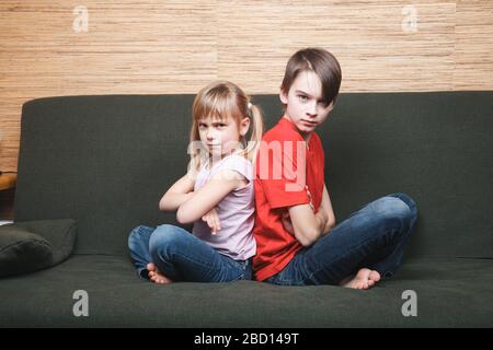 Frustrierte Geschwister sitzen auf einem Sofa, das zu Hause in Selbstisolation stecken blieb. Quarantäne und Sperrung von Schutzmaßnahmen gegen die Ausbreitung von Coronavirus Stockfoto