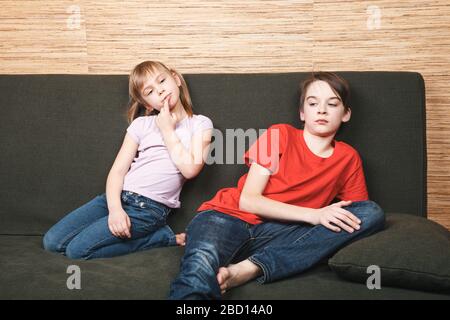 Frustrierte Geschwister sitzen auf einem Sofa, das zu Hause in Selbstisolation stecken blieb. Quarantäne und Sperrung von Schutzmaßnahmen gegen die Ausbreitung von Coronavirus Stockfoto