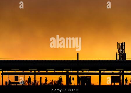 Cornbrook Straßenbahnhaltestelle in Manchester bei Sonnenuntergang, mit nahe gelegenen Moorland Waldbrände geben den Himmel ein orange leuchten Stockfoto