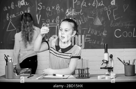 Schüler im Chemieunterricht am Schwarzen Brett. Laborpraxis. Chemieklassen. Faszinierende Wissenschaft. Bildungsexperiment. Mädchen Klassenkameraden studieren Chemie. Mikroskopteströhrchen chemische Reaktionen. Stockfoto