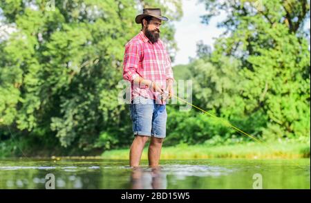 Irgendeine Art von Meditation. Fische, die normalerweise in freier Wildbahn gefangen werden. Forellenfarm. Fischer allein stehen im Flusswasser. Mann bärtiger Fischer. Angelausrüstung für Fischer. Hobbysport-Aktivität. Ruhige und friedliche Stimmung. Stockfoto