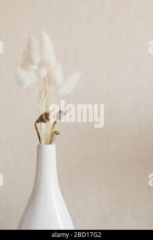 Trockene Blumen in Keramik-Vase weiß. Einrichtung im skandinavischen Stil. Beigefarbener Hintergrund Stockfoto